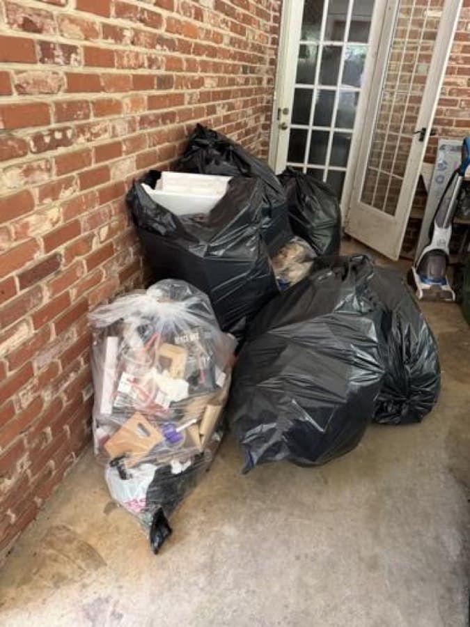 Bagged household junk staged for pickup next to a brick exterior